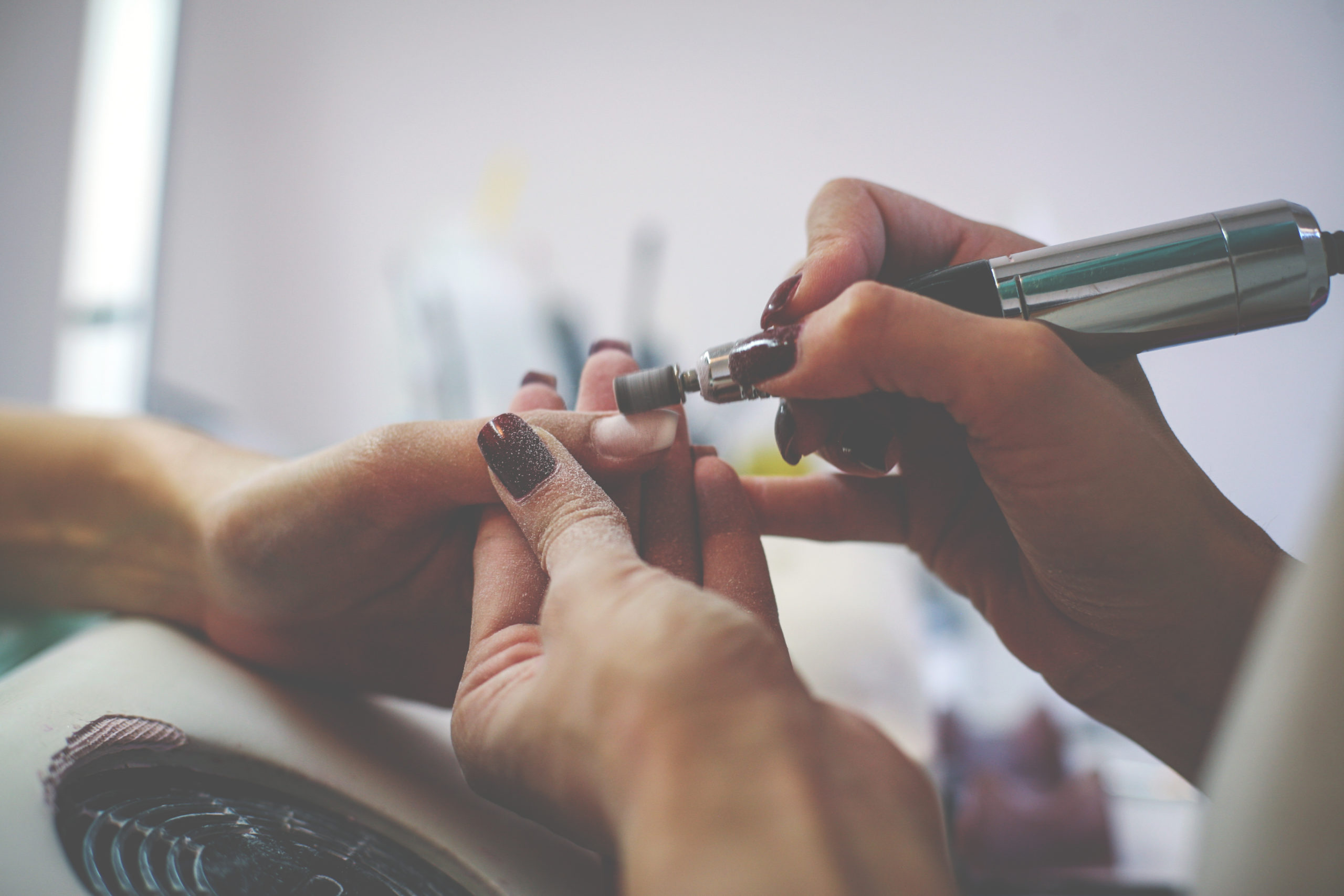 The process of manicure at a beauty salon with electrical  file.  Close up.